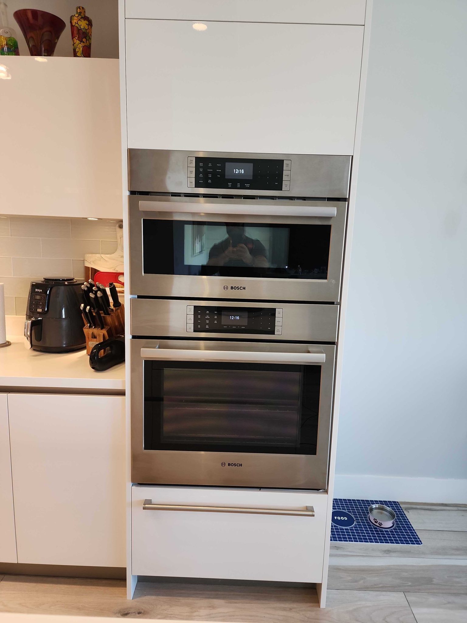 Front view of a stainless steel Bosch built-in microwave and wall oven combination unit installed in white kitchen cabinetry.