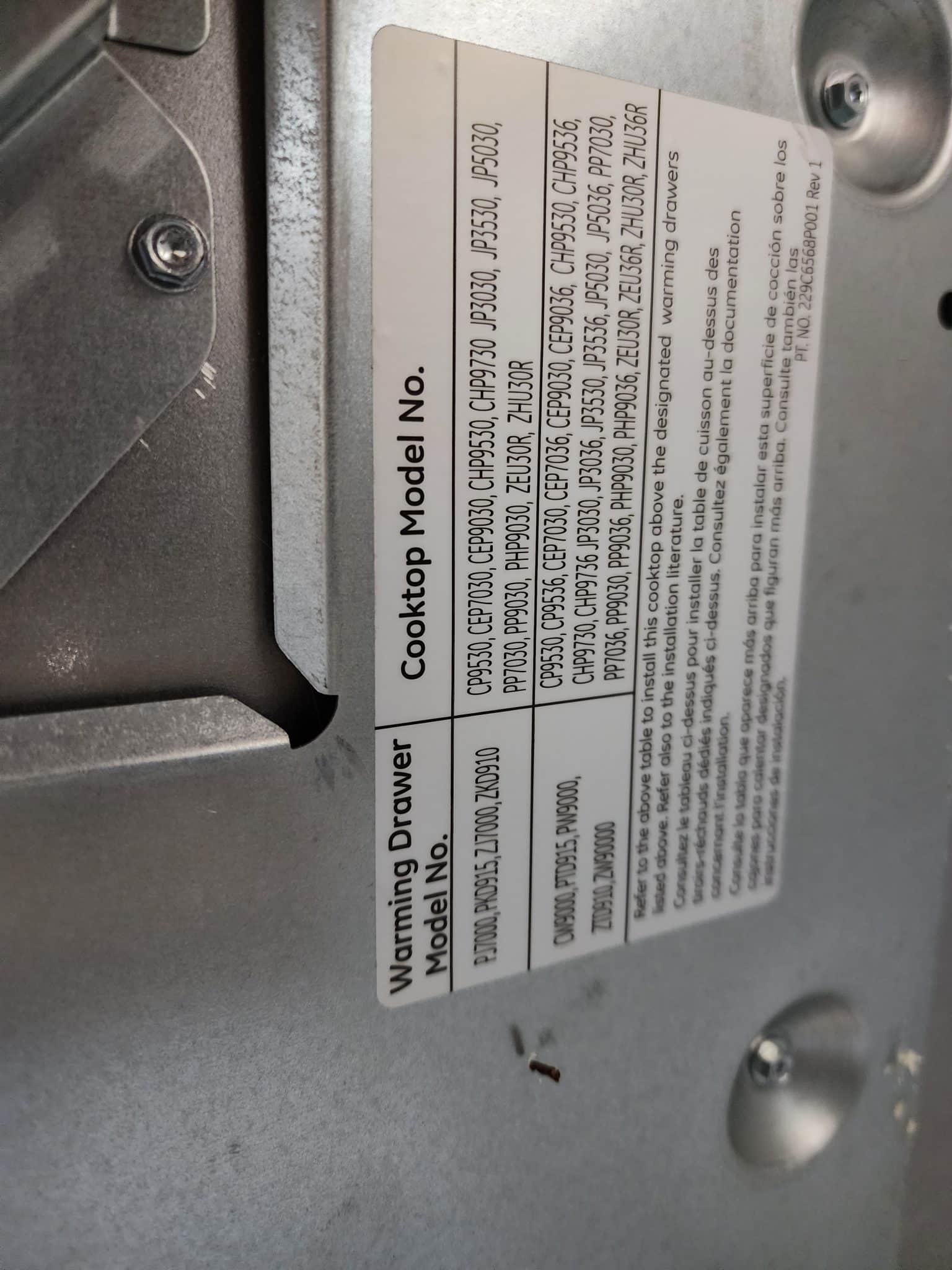 Close-up of the manufacturer specification sticker located underneath the appliance, displaying a list of cooktop and warming drawer model numbers.
