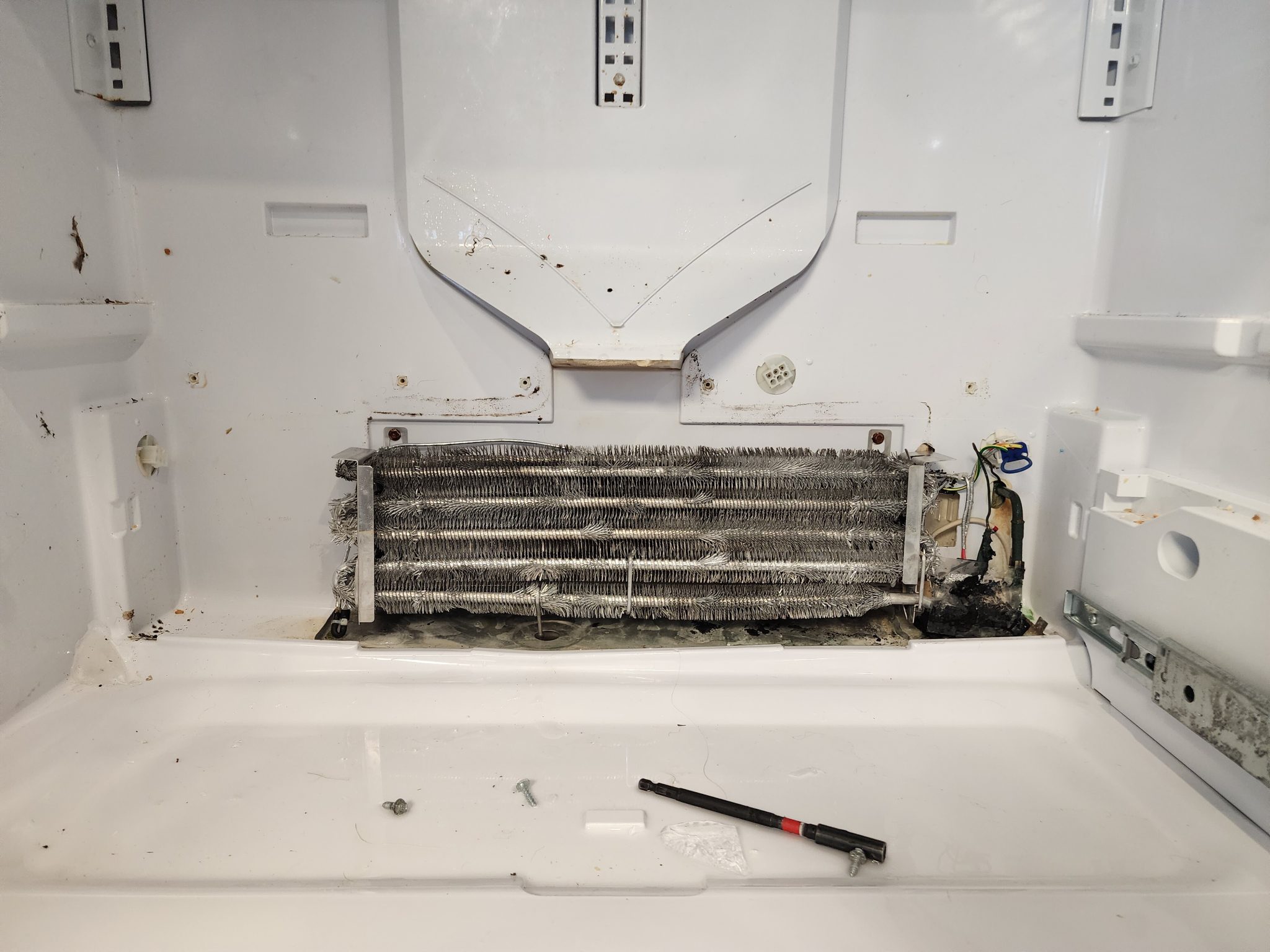 Interior view of a disassembled GE Profile refrigerator model PYE22PSKNSS showing dual-stacked evaporator coils with melted wiring and severe burnt debris on the upper right side.