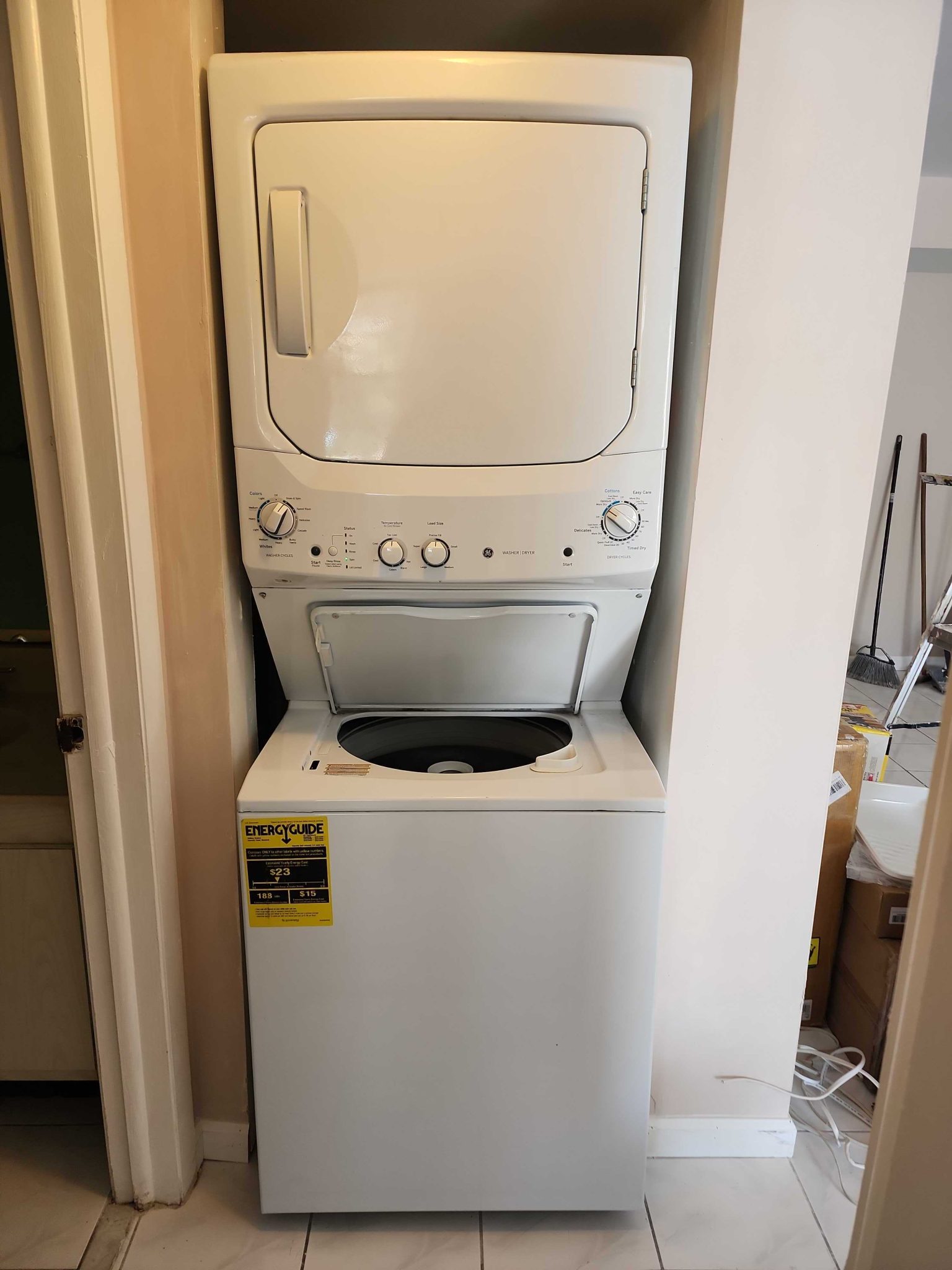 Front view of a white GE stackable washer and dryer laundry center installed in a utility closet with the washer lid open.