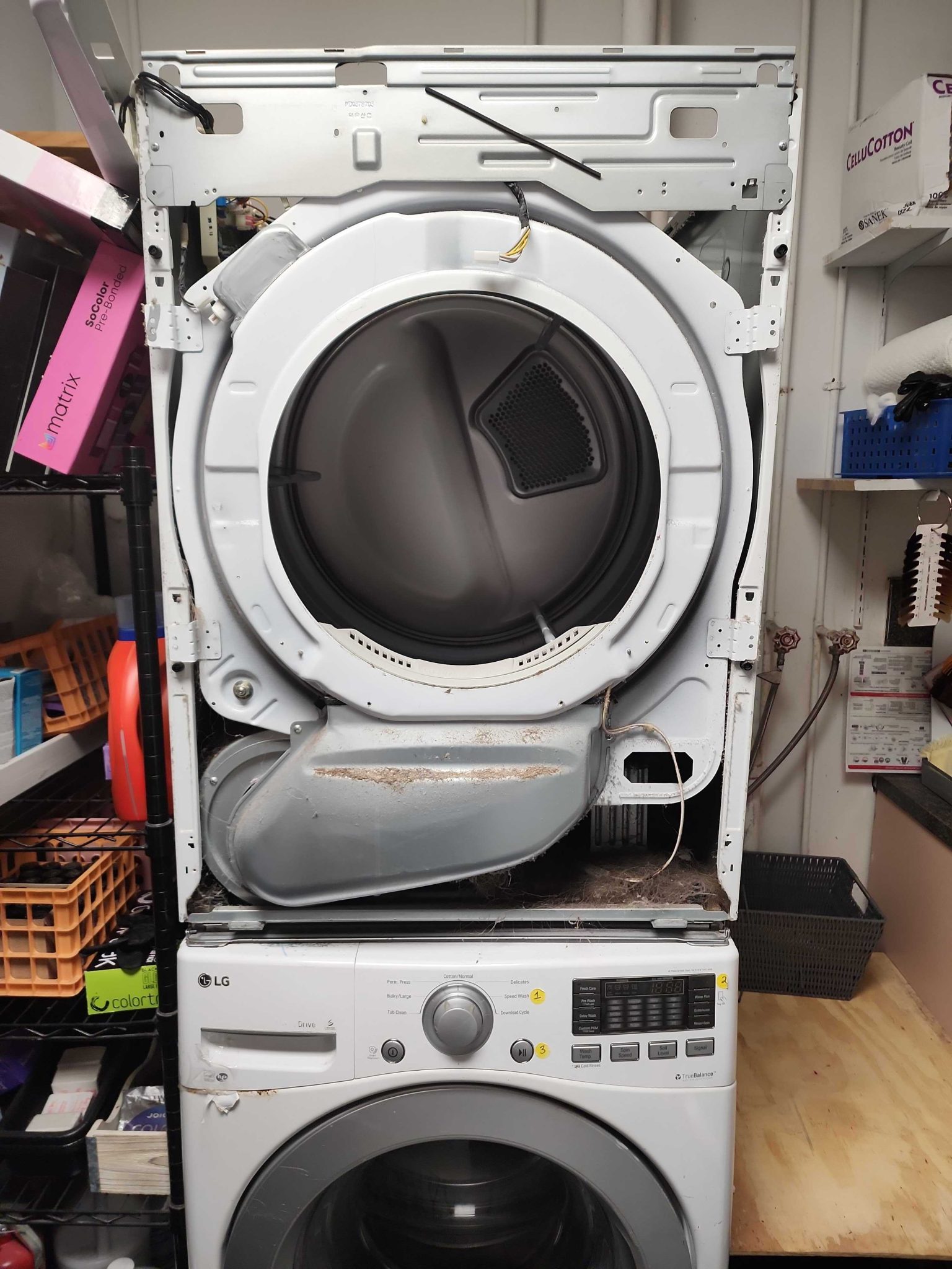 Front view of a disassembled white LG dryer stacked on top of a washer in a commercial salon setting, showing the exposed internal drum, blower housing, and accumulated lint before the moving parts were replaced.