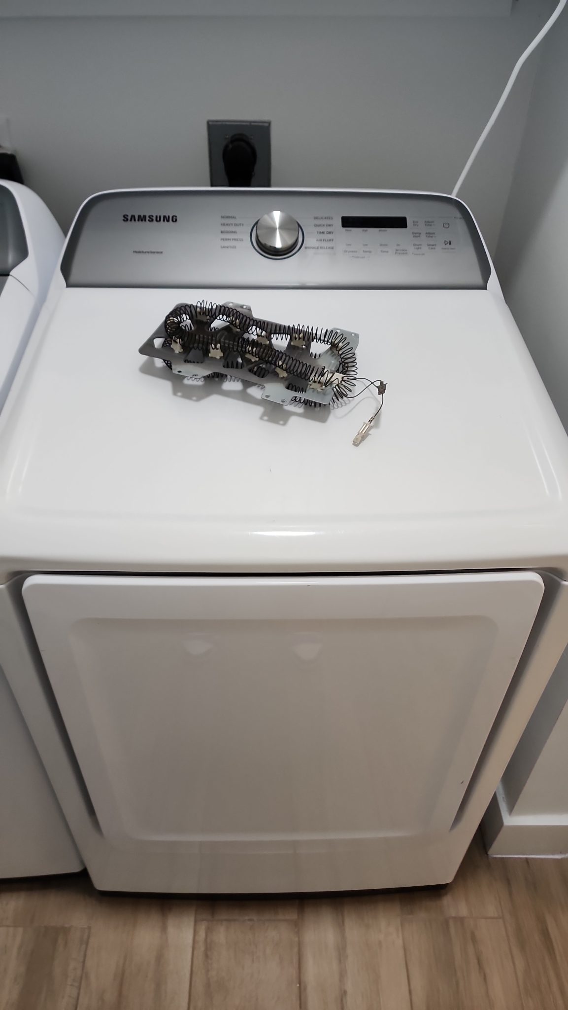 Front view of a white Samsung electric dryer in Tamarac, FL with a failed heating element assembly resting on top after repair.