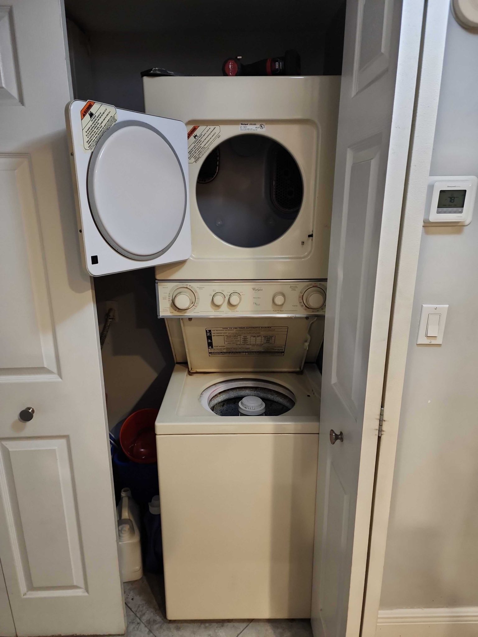 Front view of an older model Whirlpool stacked laundry center installed inside a closet with the washer and dryer doors open.